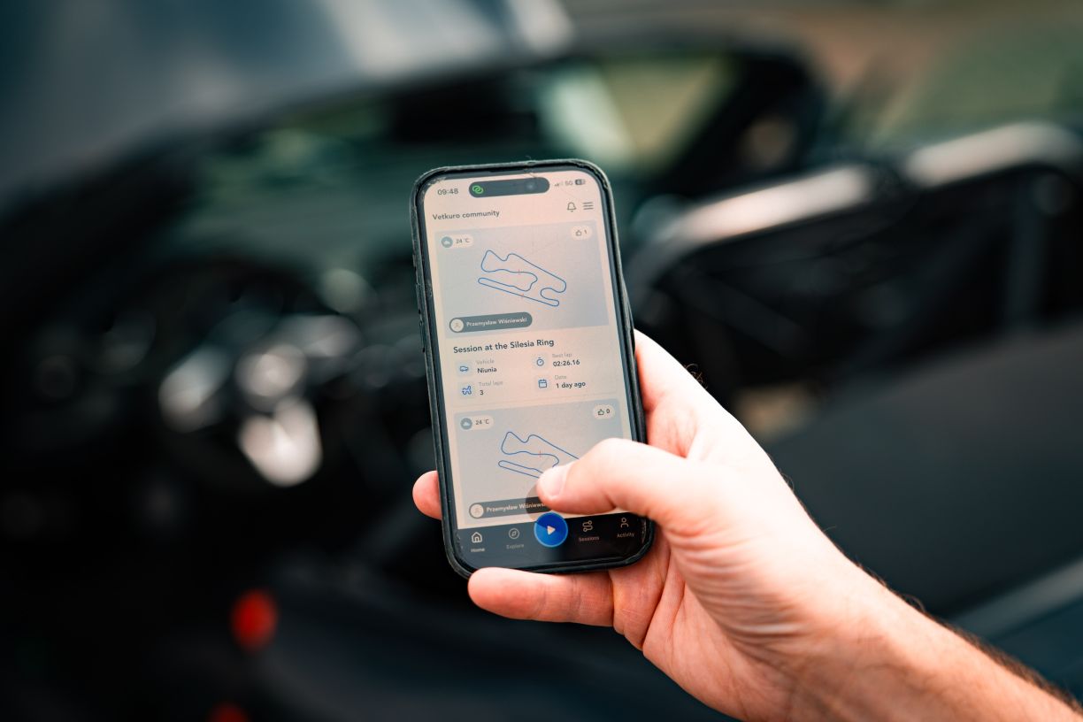 A phone running Vetkuro, held in front of a car on a track day