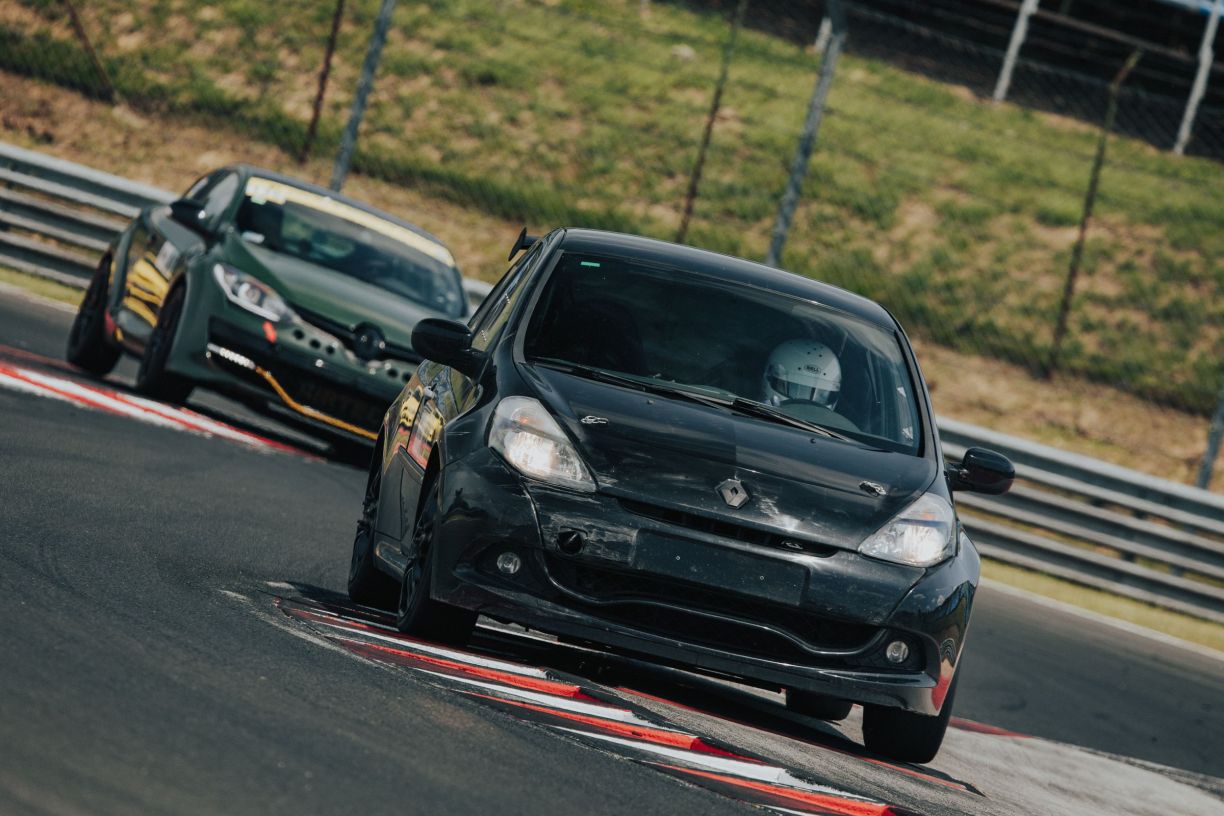 A Clio taking a corner over the kerb, a second car close behind.
